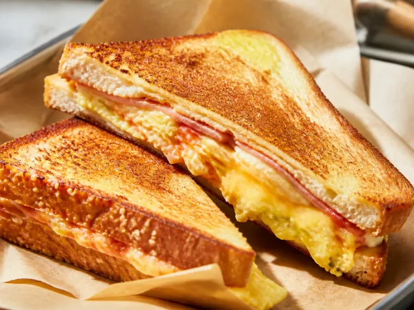 Korean street toast halved diagonally on a plate, showing melted cheese, ham, and vegetable cabbage omelette inside toasted golden bread.